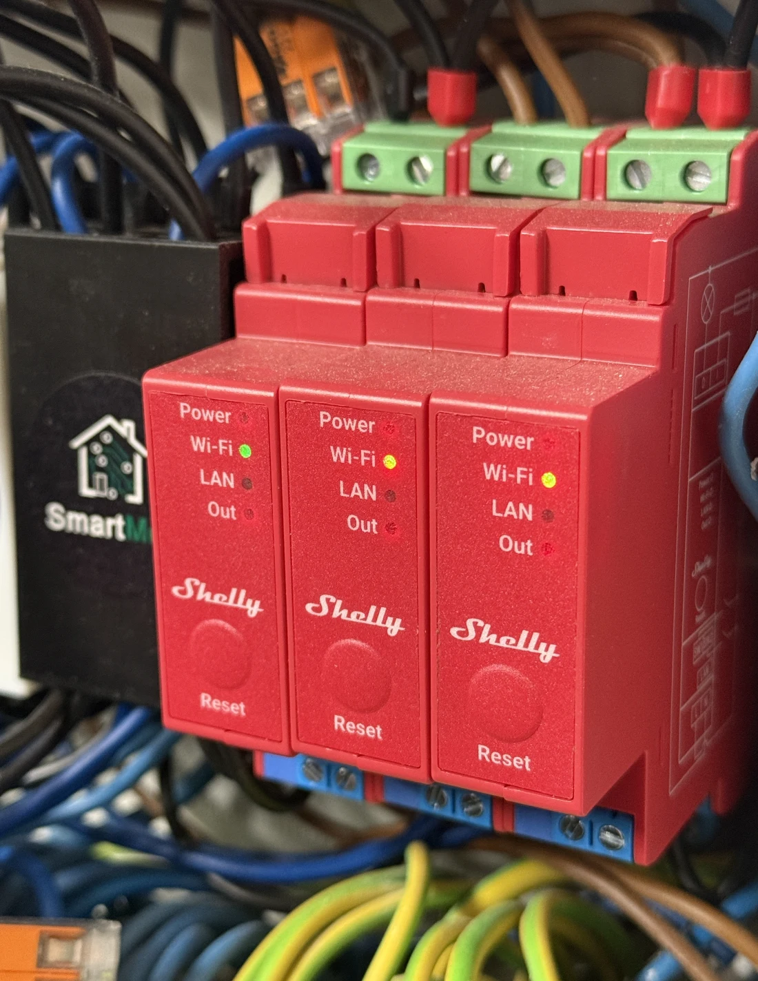 Trzy moduły Shelly Pro na szynie DIN w rozdzielnicy, zainstalowane i oznaczone przez SmartMod Labs — realna instalacja, nie zdjęcie poglądowe